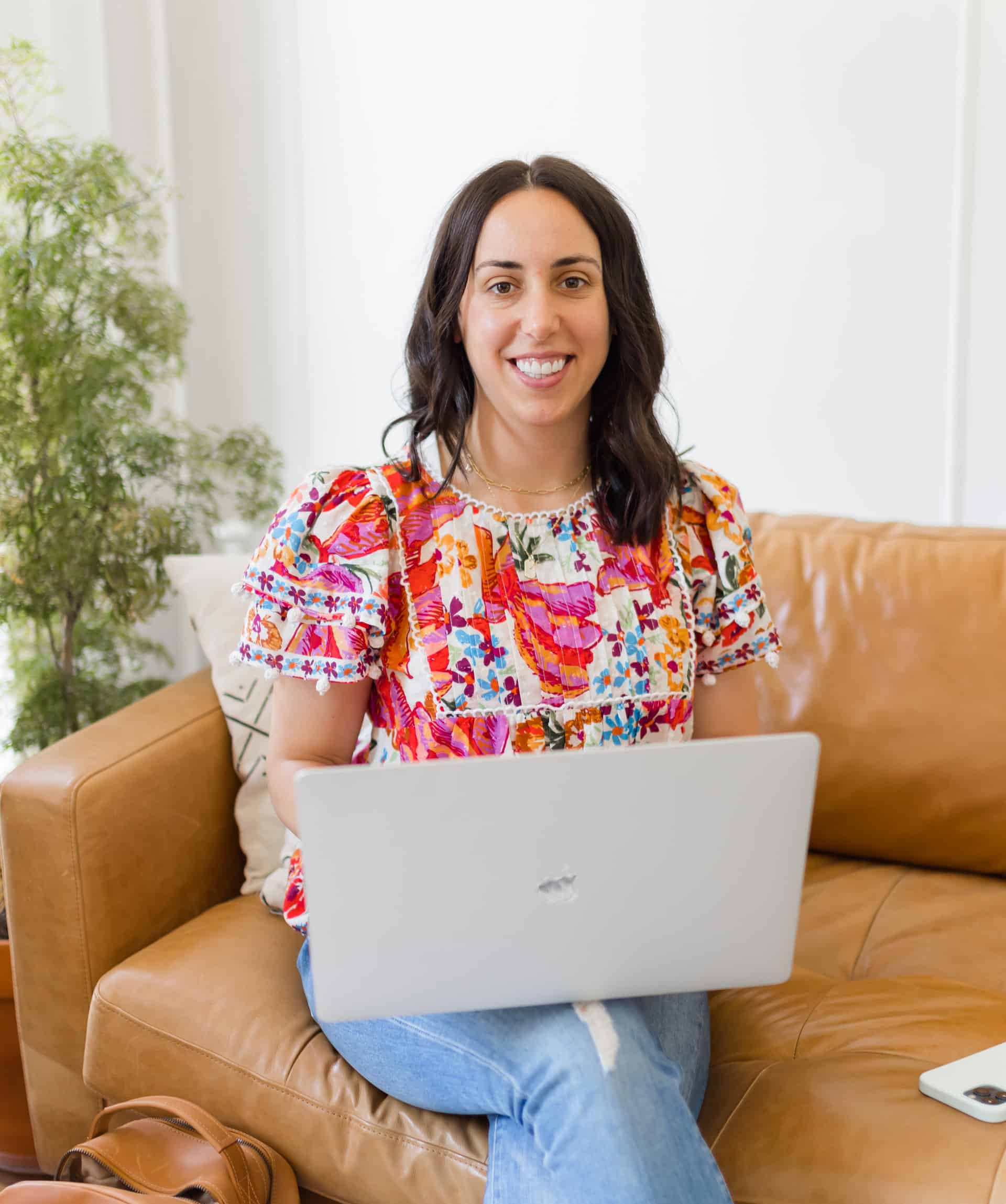 Woman with long dark hair sitting with a laptop and smiling