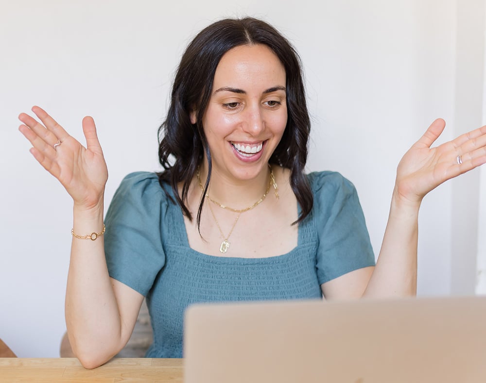 woman with dark hair smiling with laptop in front of her