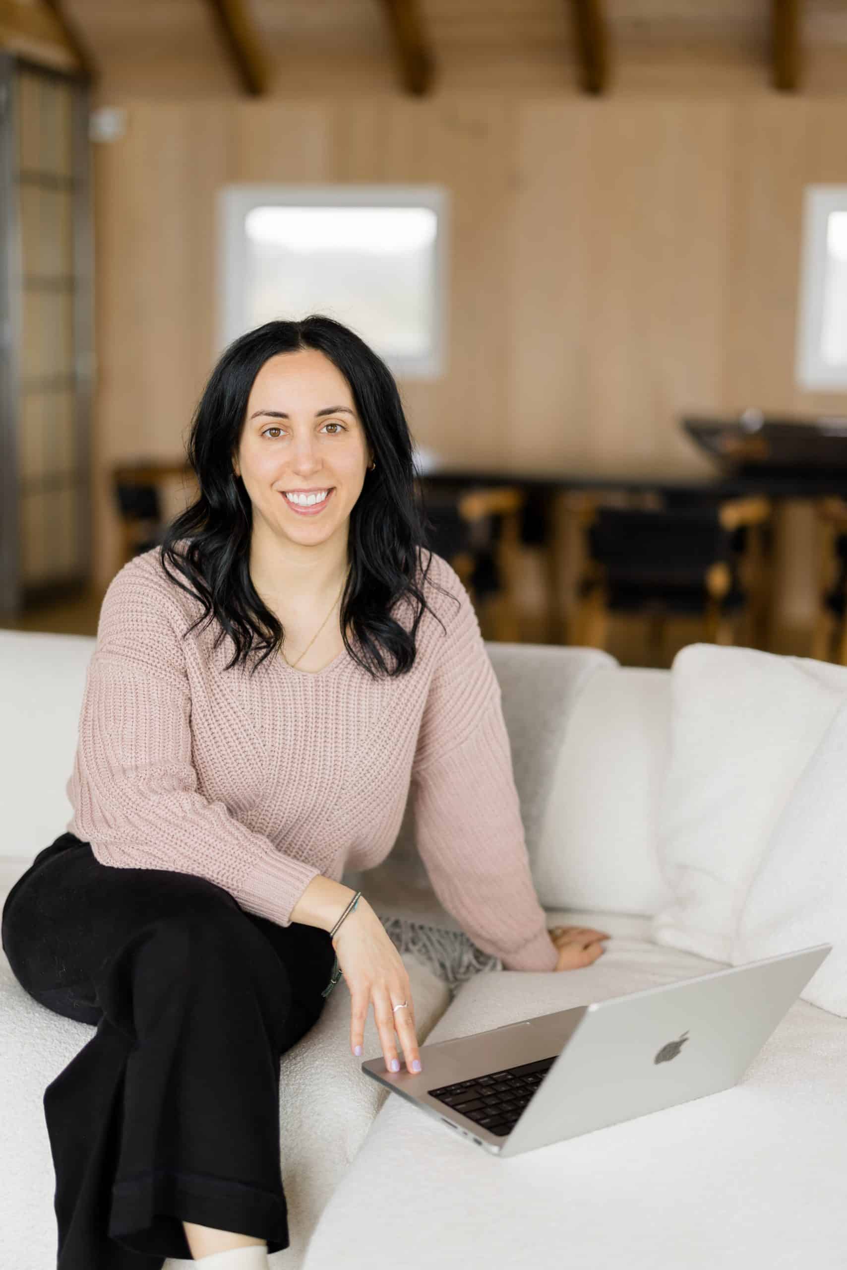 women in a pink sweater sitting on a couch working on her laptop