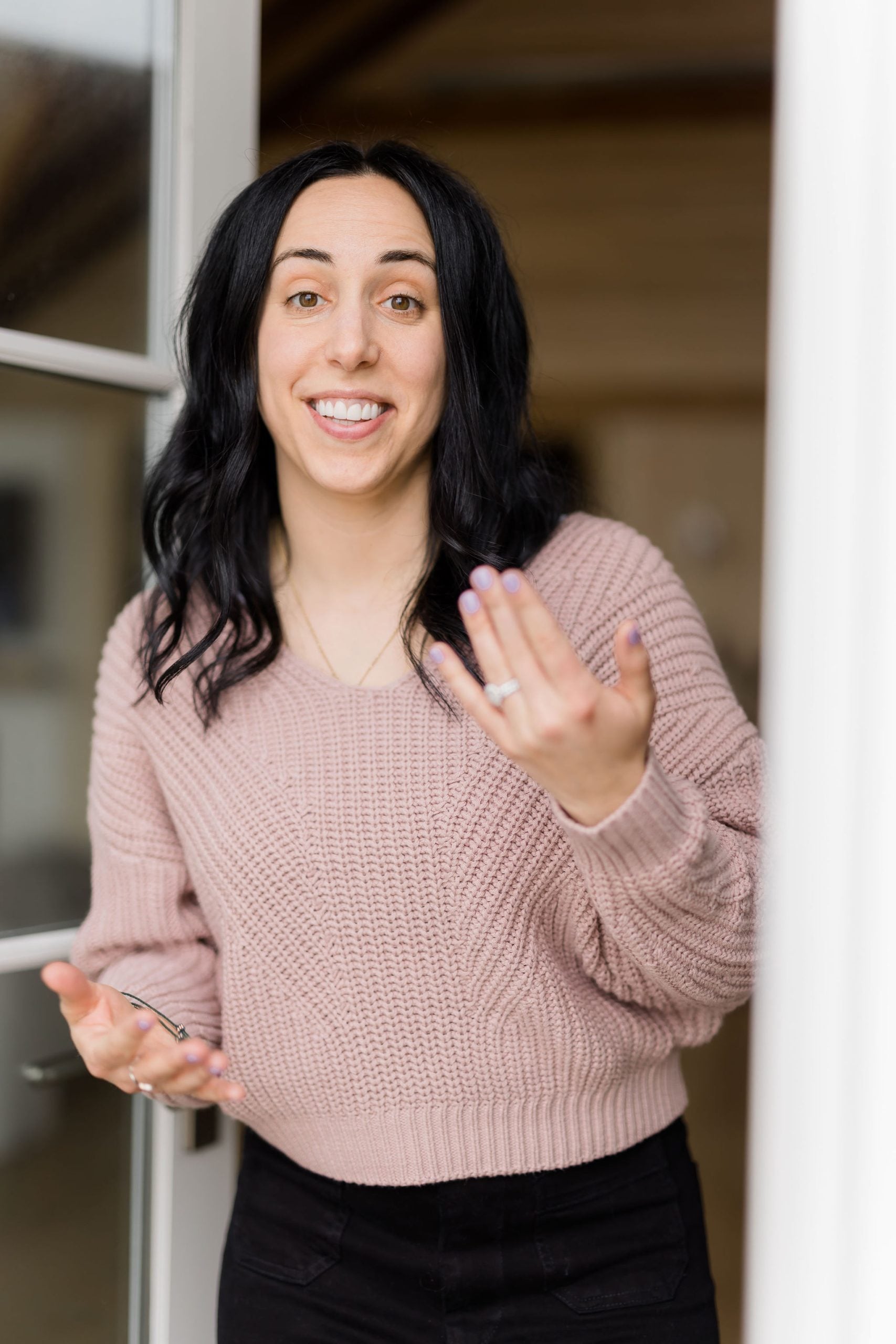 woman with dark hair smiling and welcoming to come indoors