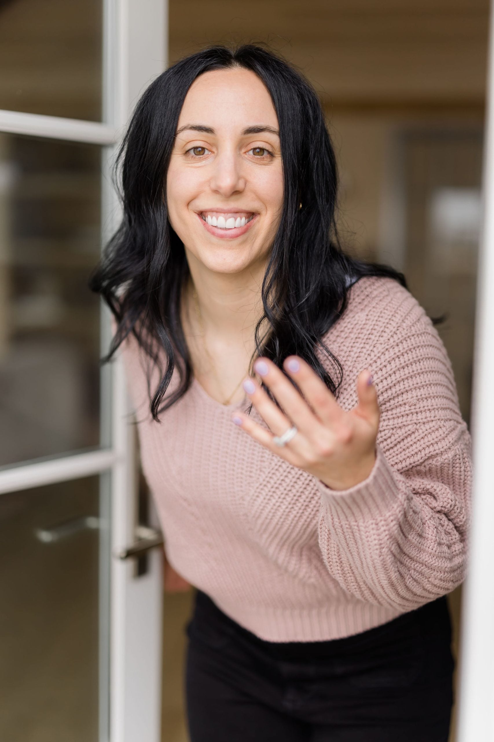 woman with dark hair smiling and welcoming to come indoors